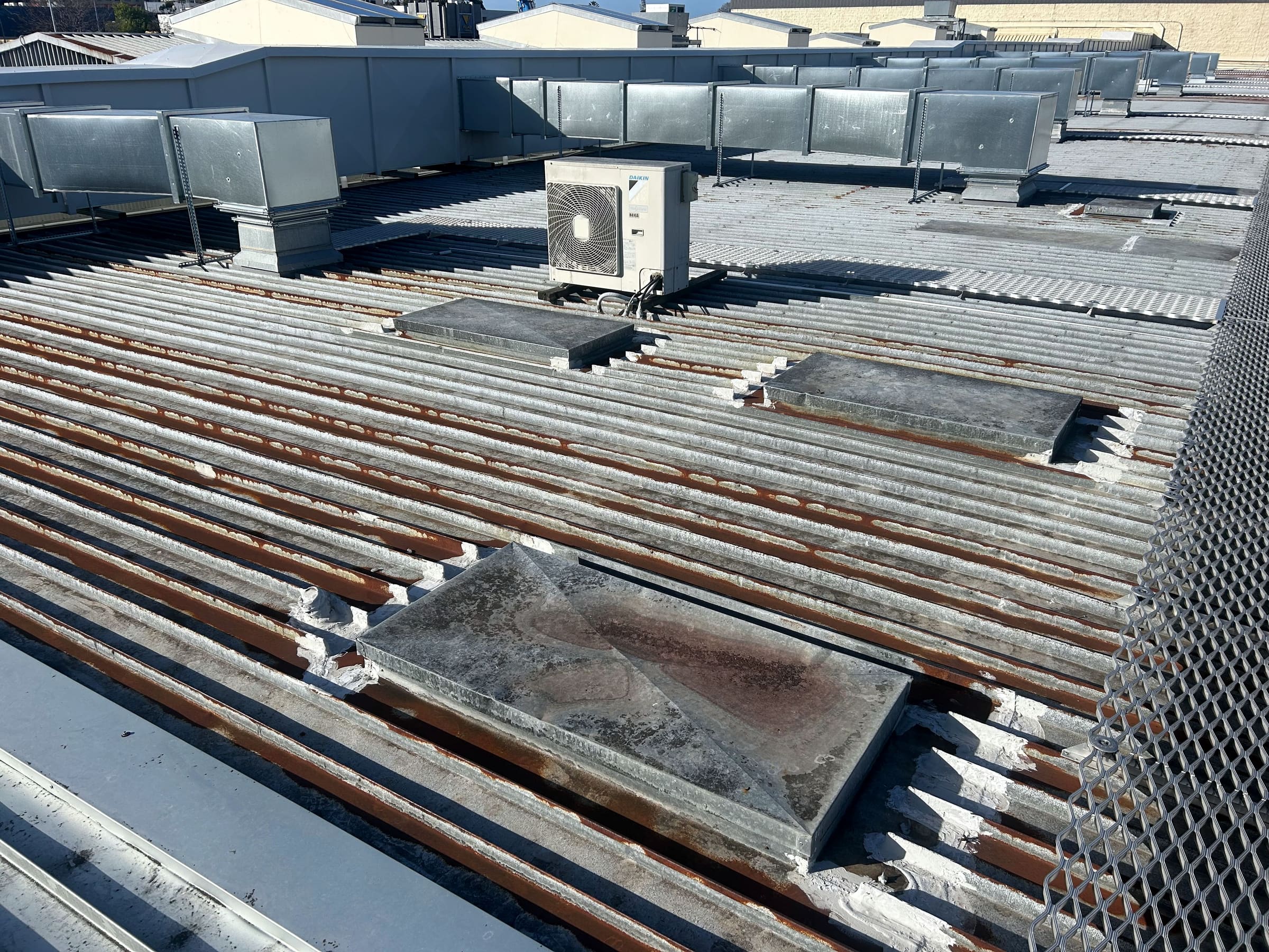 An existing commercial corrugated roof with heavy rust along the ribs and capped penetrations.