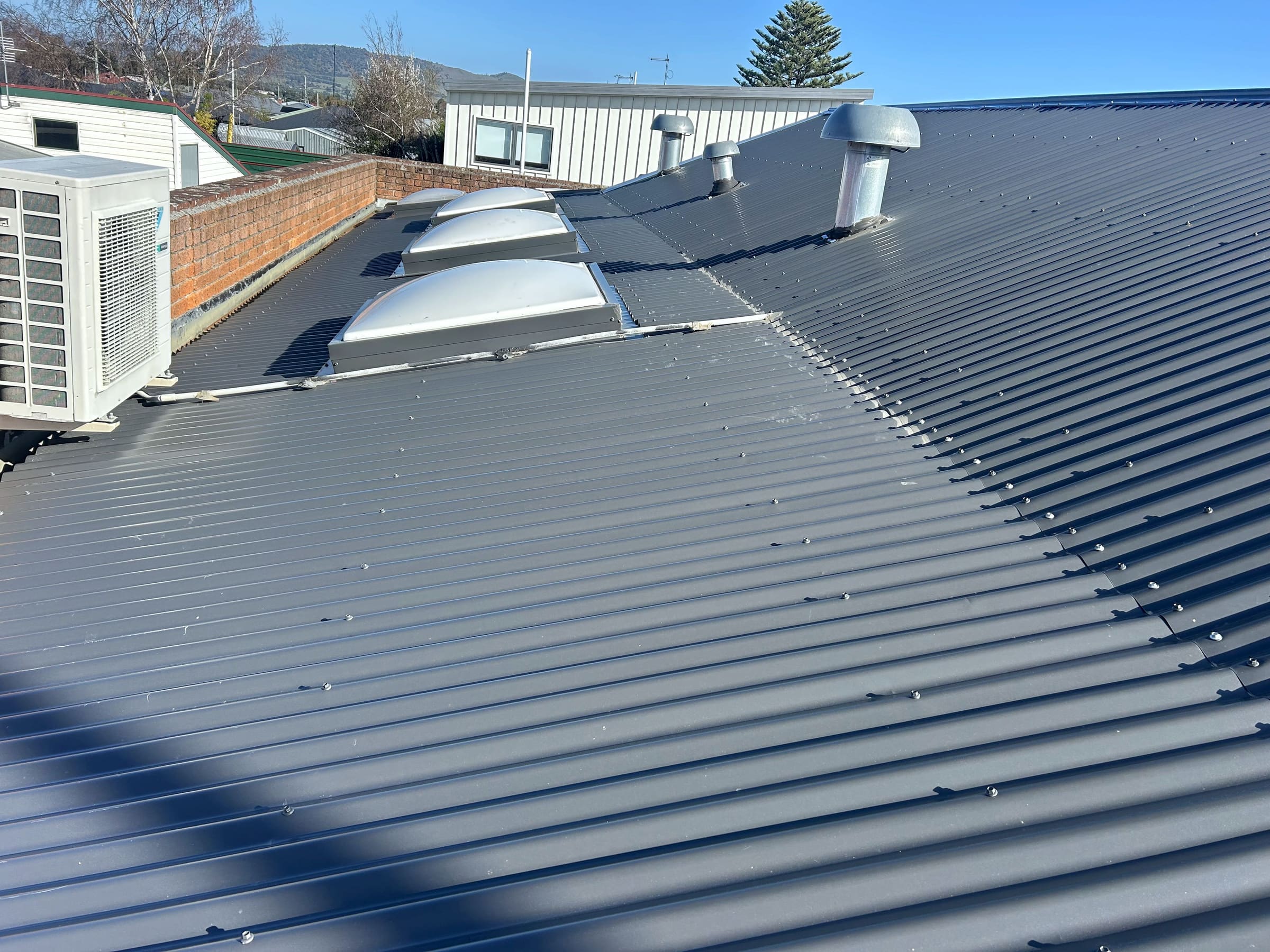 New charcoal corrugated roof with domed skylights and two cowl vents, alongside a brick parapet.
