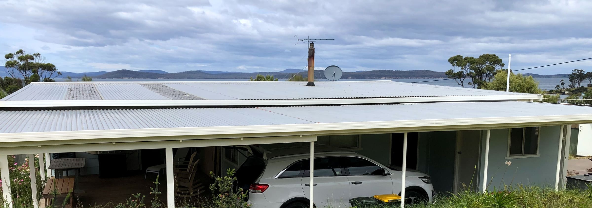 Single-storey house with a new light metal roof over the verandah and carport, water and hills behind.