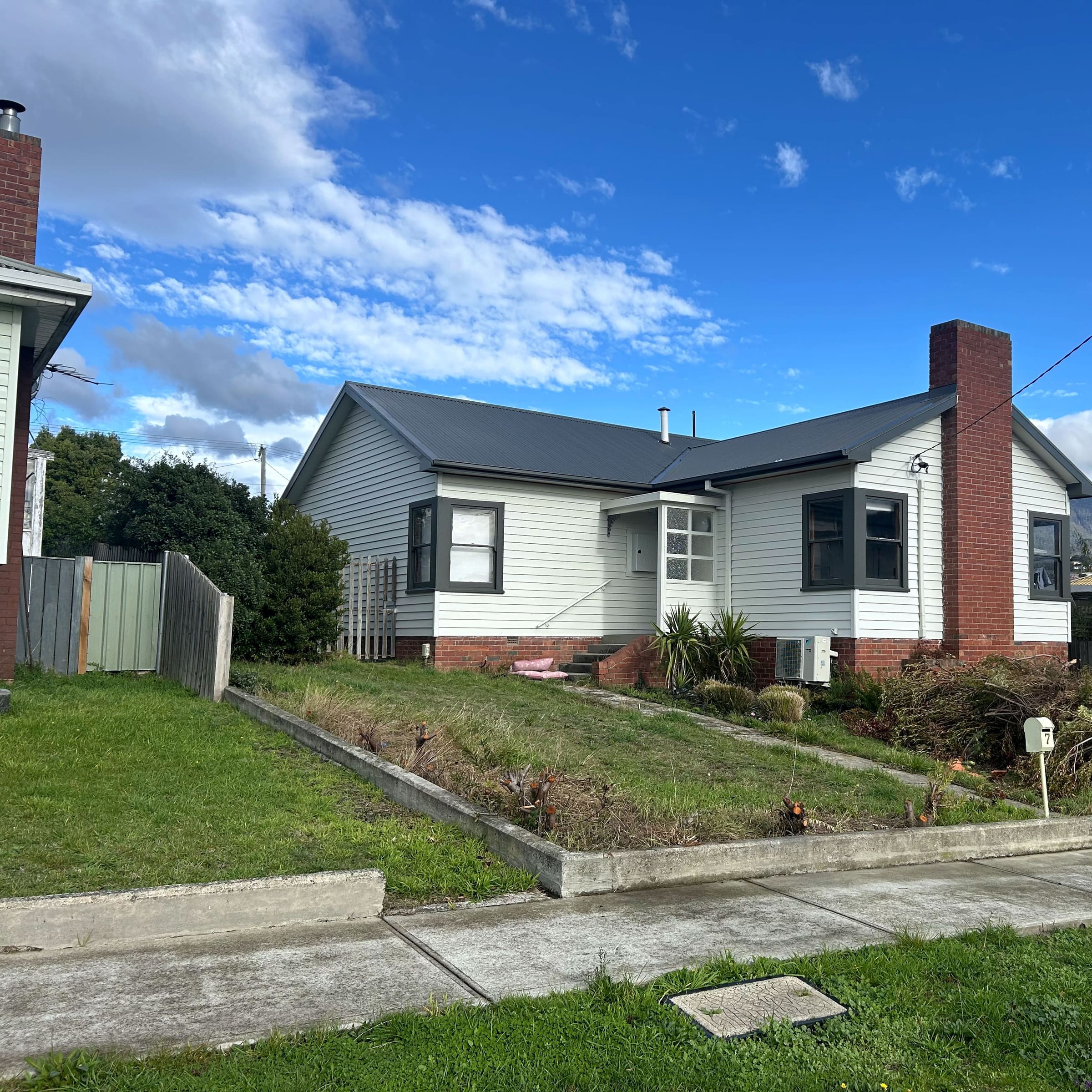Weatherboard house with a newly installed dark corrugated metal roof and matching gutters, hills behind.